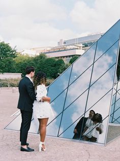 a man and woman standing in front of a building with a reflection on the wall