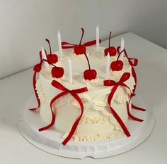 a cake with white frosting and red ribbon around it, topped with cherries