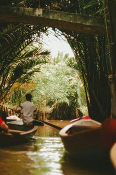 two people are riding in small boats on the water near palm trees and greenery