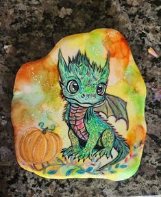 a painted rock sitting on top of a counter next to a white plate with a green dragon