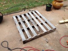 a wooden pallet sitting on top of a cement floor next to a potted plant