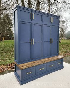 a blue armoire sitting on top of a wooden bench in front of some trees