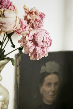 pink flowers are in a vase next to an old photograph on a shelf with a man's face