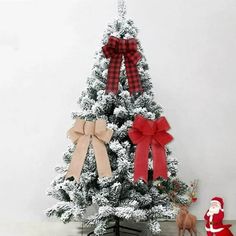 a small christmas tree with red and white bows on it's top, next to a santa clause figure