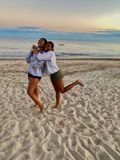 two young women are hugging on the beach