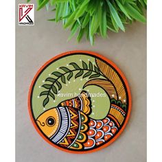 an orange and green fish design on a round mat next to a plant with leaves