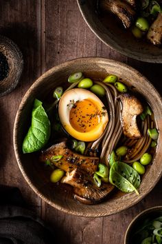 two bowls filled with food on top of a wooden table next to green vegetables and bread