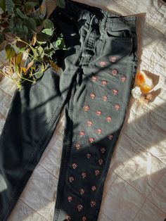 a pair of black jeans with red flowers on them sitting on a bed next to a potted plant