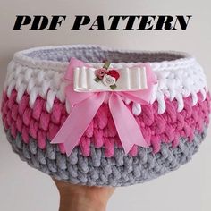 a hand holding up a basket with pink and white yarn on it, the bottom has a bow