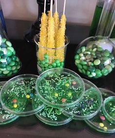 green and yellow candies in plastic bowls on a table with candy sticks, bottles and vases