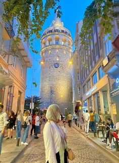 a woman is standing in the middle of an alley way with many people walking around