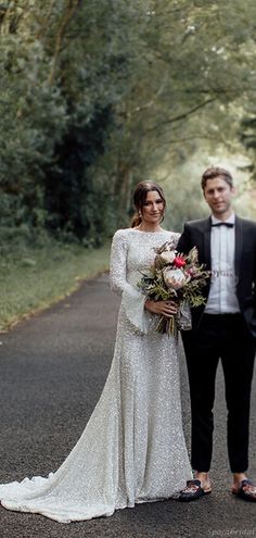 a bride and groom standing in the middle of an empty road with trees on either side