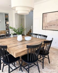 a dining room table with black chairs and a white vase on the centerpiece in front of it