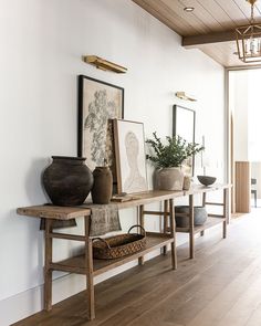 a wooden table topped with vases sitting on top of a hard wood floor next to a white wall