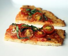 two slices of pizza with tomatoes and basil on them sitting on a white table top