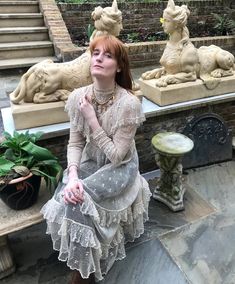 a woman sitting on top of a stone bench next to statues and planter pots