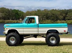 a blue and white truck parked on top of a grass covered field next to a lake