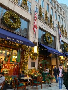 people walking down the sidewalk in front of a building with christmas decorations and wreaths