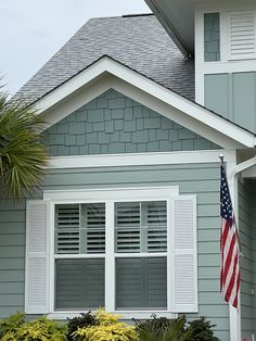 an american flag is in front of a gray house with white shutters and windows