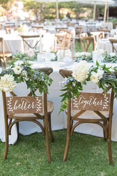 two wooden chairs with white flowers and greenery are set up for an outdoor reception