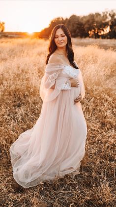 a pregnant woman standing in a field with her hands on her stomach wearing a white dress