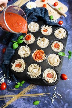 cupcakes with sauce being poured on them in a muffin tin, next to tomatoes and basil