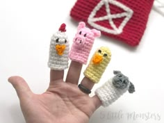 a hand is holding five tiny crocheted finger puppets with farm animals on them