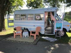 an old camper is parked in the grass with lawn chairs and tables around it