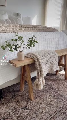 a wooden bench sitting on top of a rug next to a bed with white sheets and pillows