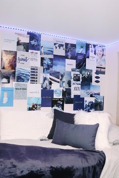 a white bed topped with pillows under a wall covered in pictures and lights next to a night stand