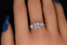 a woman's hand with blue nails and a ring on her finger, showing the three stone engagement ring