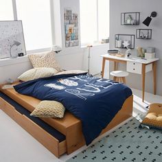 a bed with blue sheets and pillows in a room next to a desk, chair and window