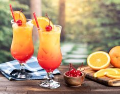 two glasses filled with orange juice and garnished with cherries on a wooden table