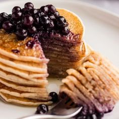 a stack of pancakes with blueberries is on a plate and has a fork next to it