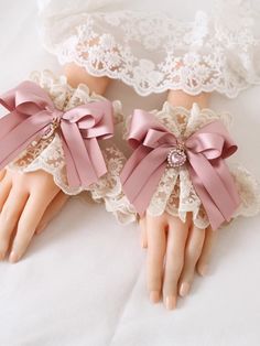 two doll hands with pink bows and laces on top of white sheets, one holding the other's hand