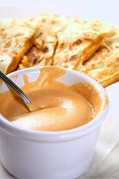 a bowl filled with liquid next to some quesadillas on a white plate