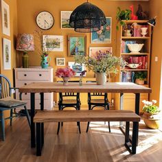 a table with two benches and some pictures on the wall behind it in a room that has yellow walls