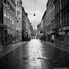 a black and white photo of an empty city street in the rain with buildings on both sides