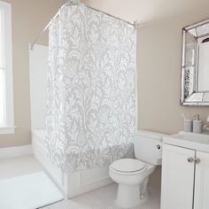 a white toilet sitting next to a bath tub under a bathroom window with a shower curtain