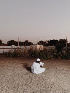 a person sitting on the ground with a book in their hand and wearing a white outfit