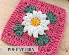 a crocheted square with a flower on it, sitting on a table top