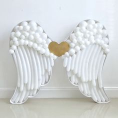 two white angel wings with gold heart on them, against a white wall and floor