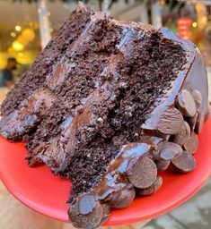 a piece of chocolate cake on a red plate with some chocolate chips around the edge