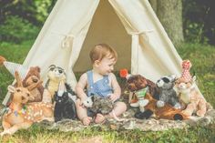 a little boy sitting in front of stuffed animals and a teepee with a tent behind him