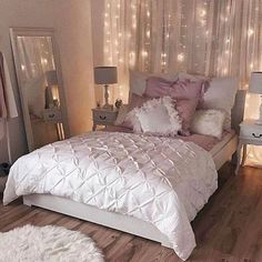 a white bed sitting in a bedroom next to a window filled with curtains and lights