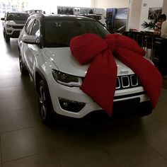 a white jeep with a red bow on it's hood in a showroom