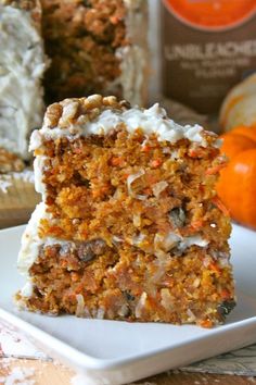 a slice of carrot cake on a white plate next to an orange and brown pumpkin