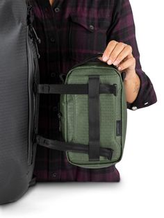 a man is holding a green bag with black straps and it's zipper open