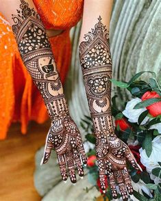 a woman's hands with henna tattoos on her arm and hand, sitting next to flowers