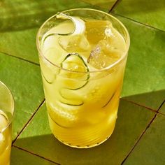 two glasses filled with lemonade and cucumber on top of a green tile floor